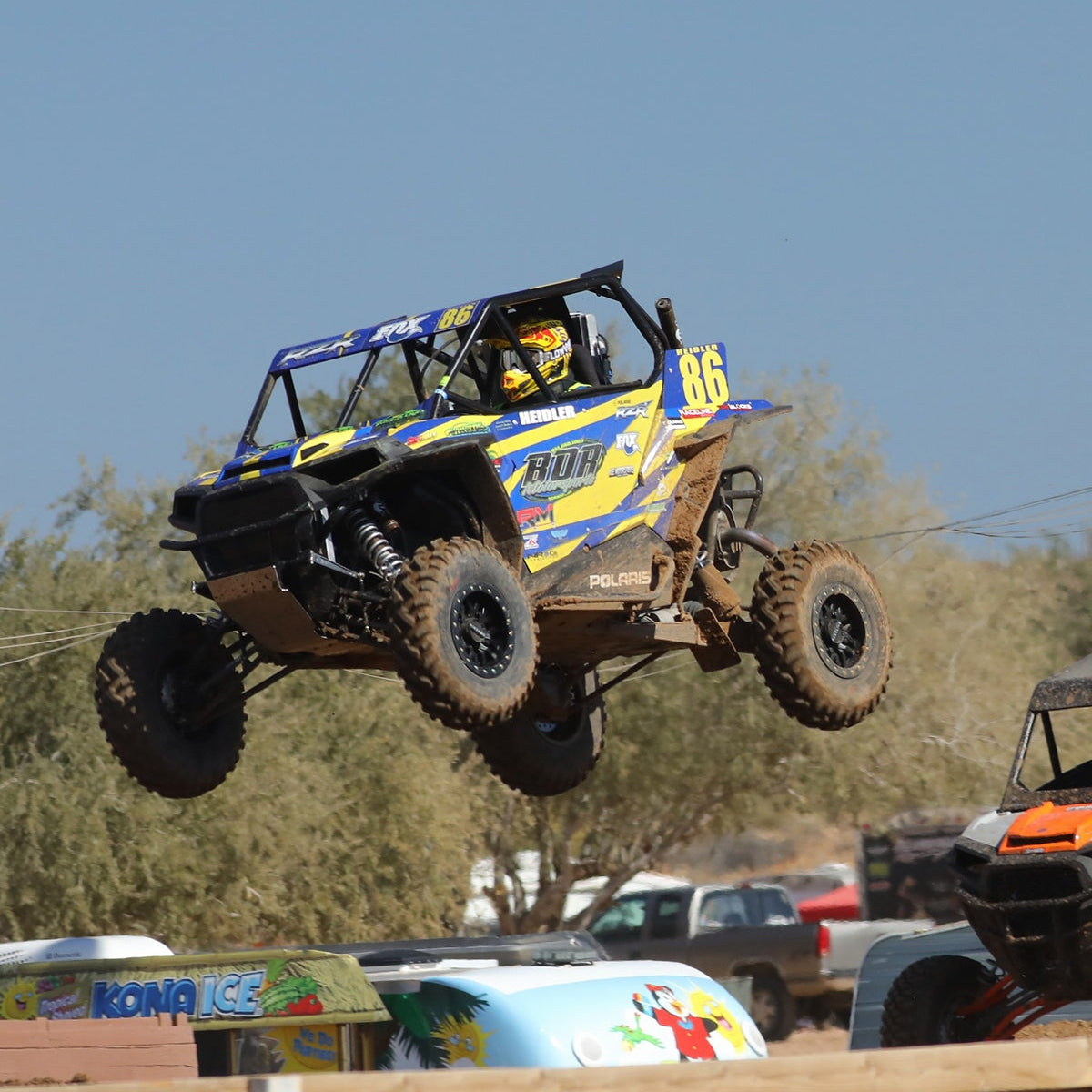 Blue Polaris RZR jumping with knobby tires and black beadlock wheels
